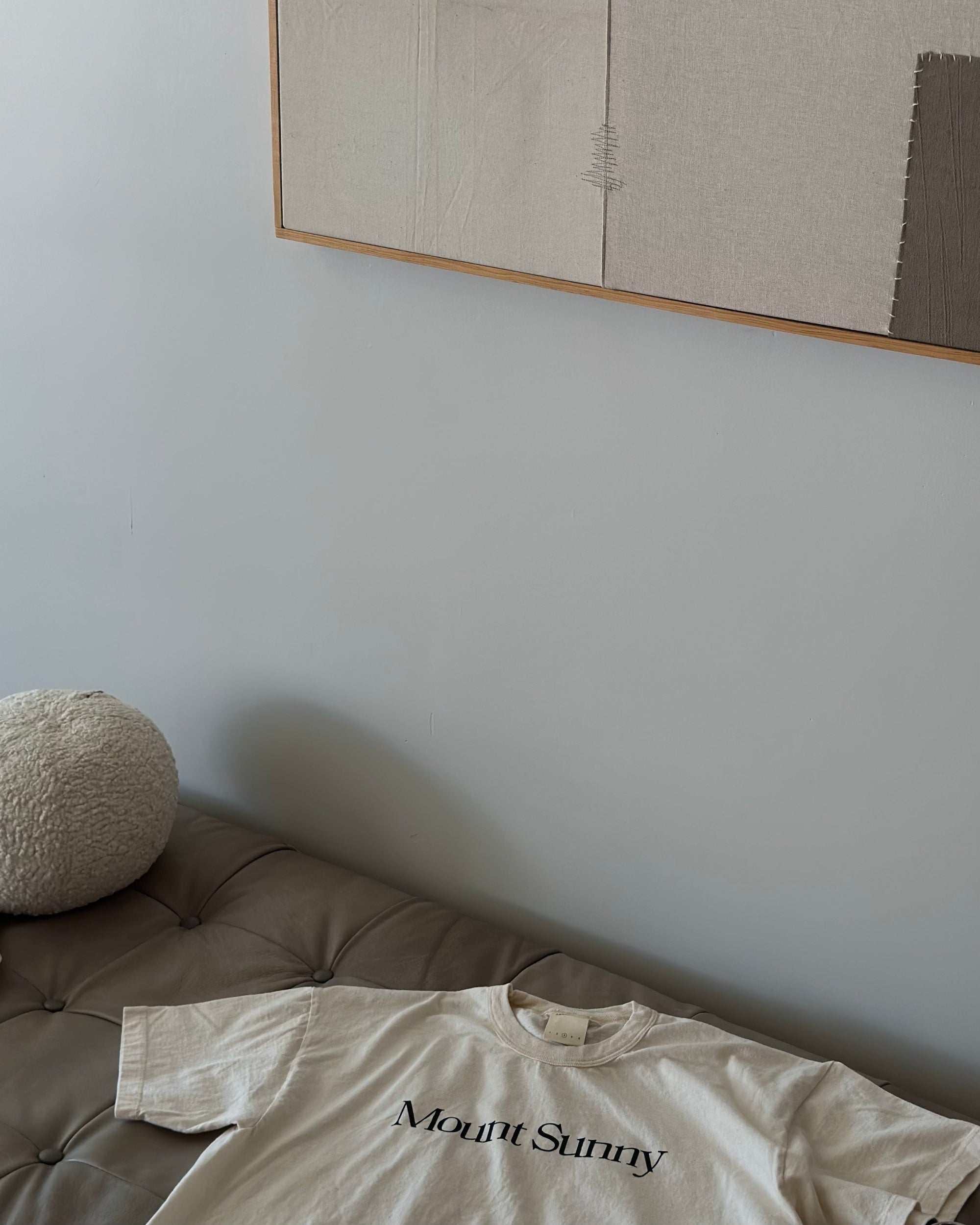 An organic cotton t-shirt laying on a daybed underneath a piece of art.