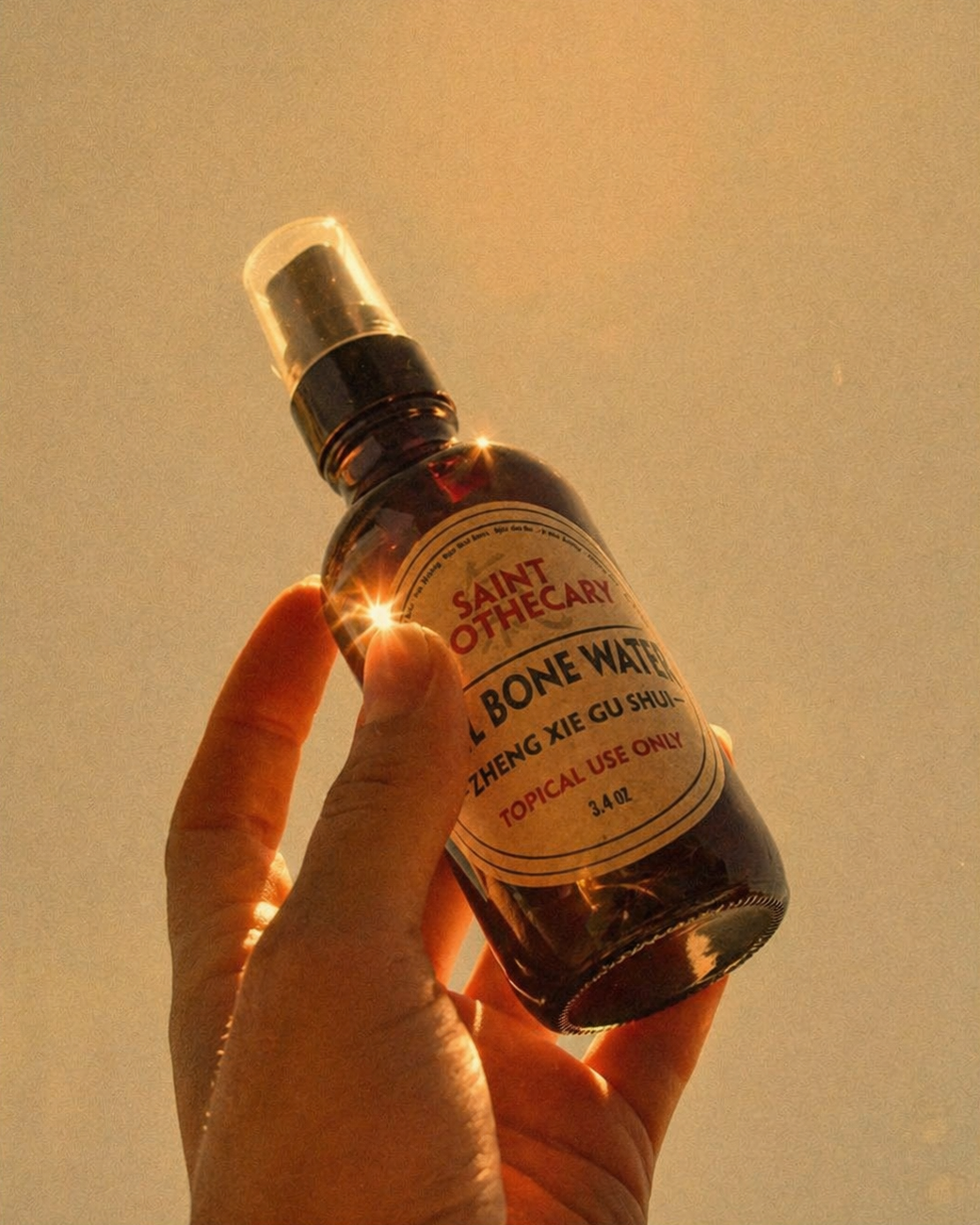 Hand holding a bottle labeled 'Saint Otherwise Bone Water' against a warm, blurred background